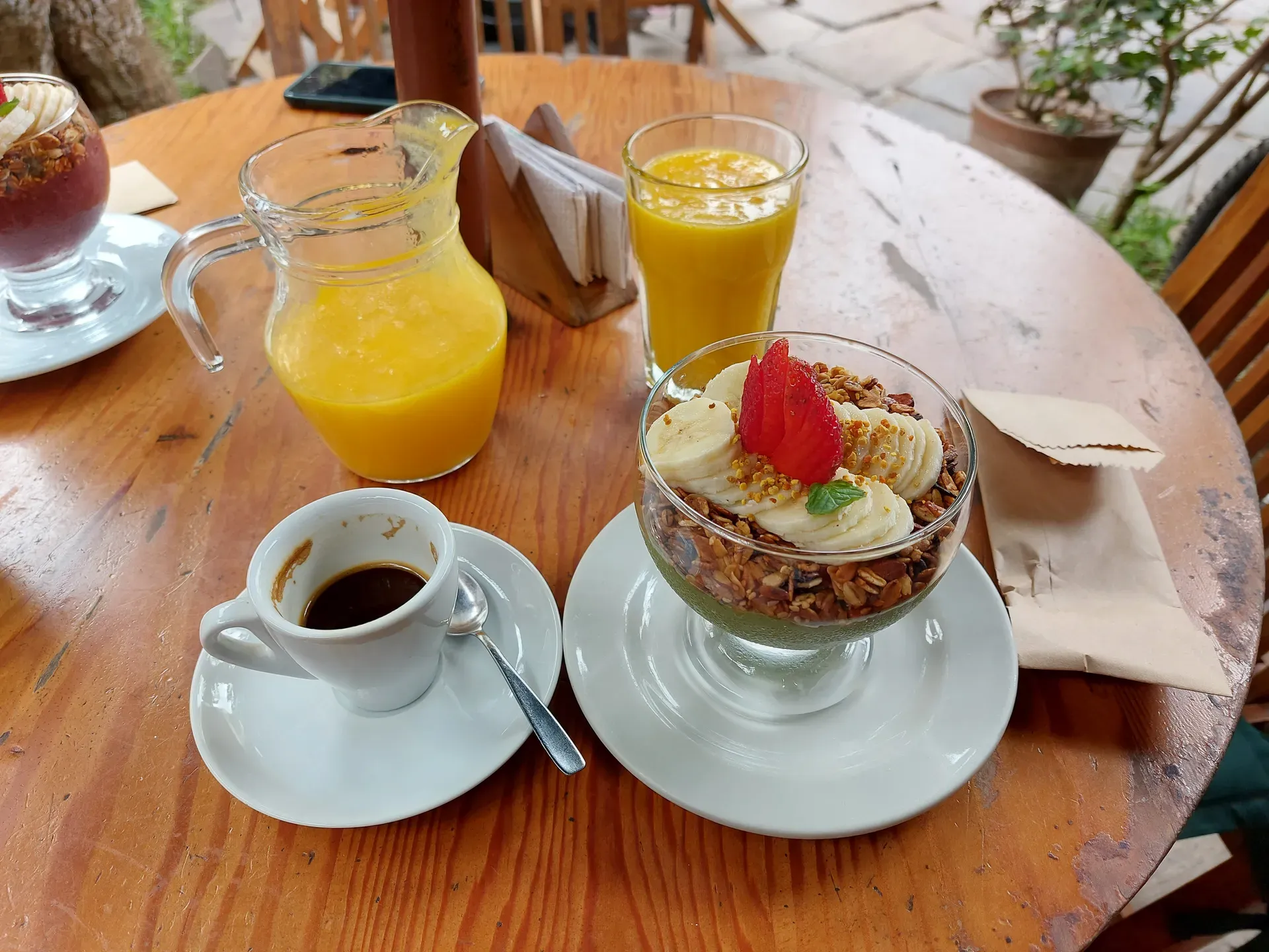 Acai and smoothie bowls with fresh fruit, granola, juice, and coffee on a wooden table in morning light.
