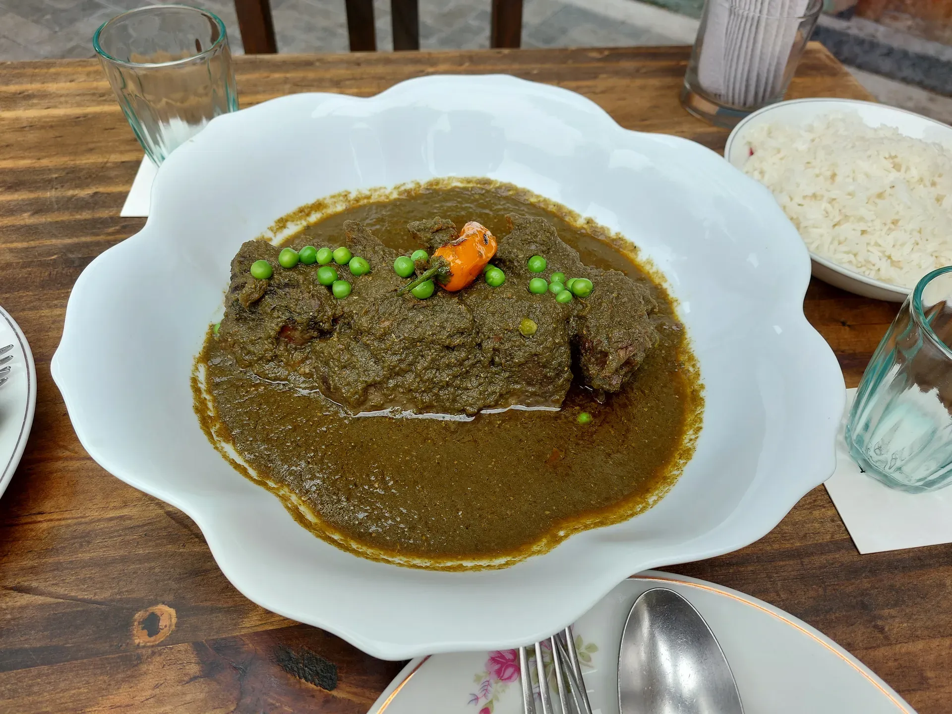 Seco-style stew in a green cilantro sauce with braised meat, peas, chili, and a side of white rice on a rustic wooden table.