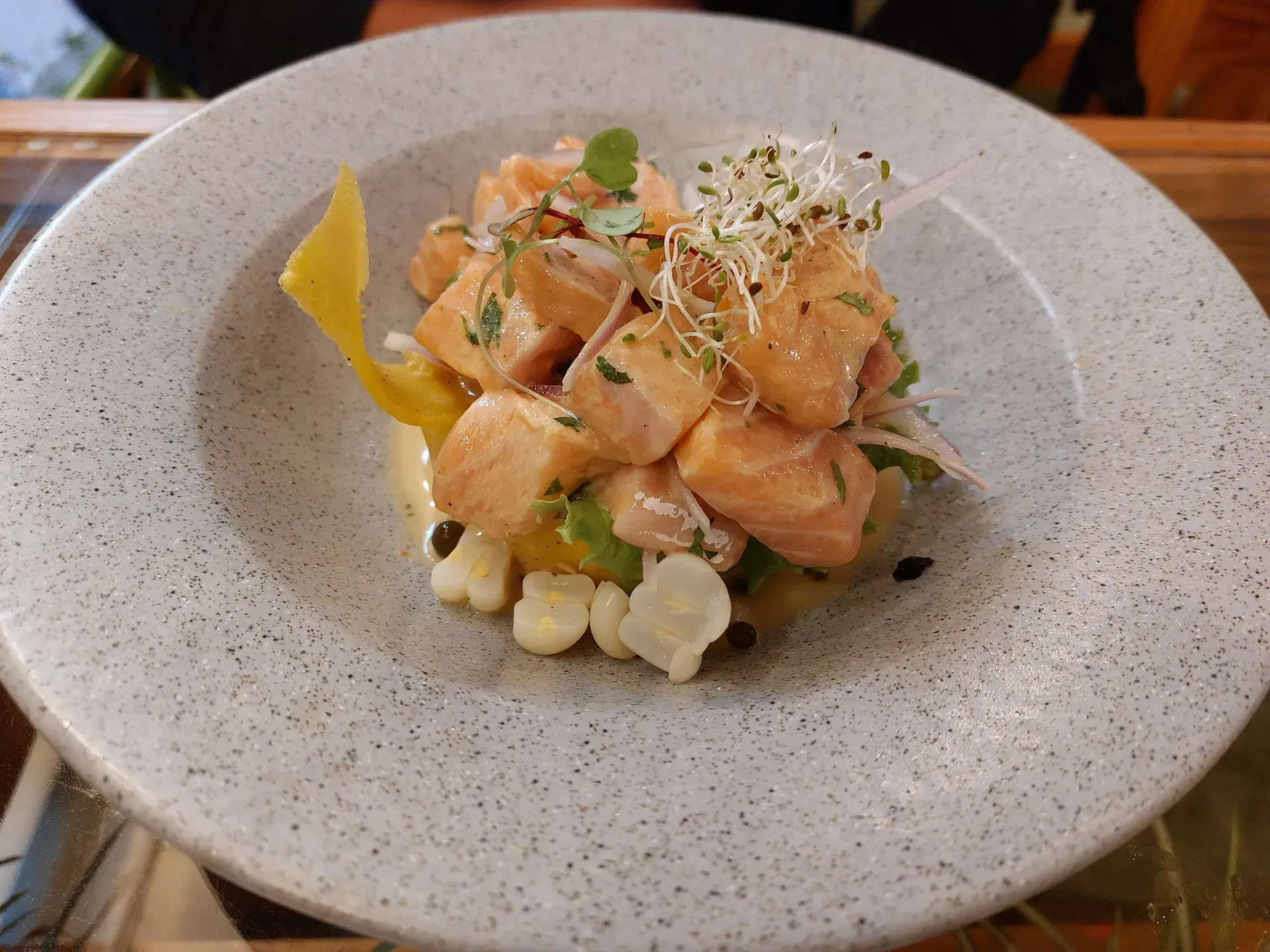 Ceviche with coral-colored fish, choclo, red onion, sprouts, and leche de tigre in a speckled ceramic bowl.