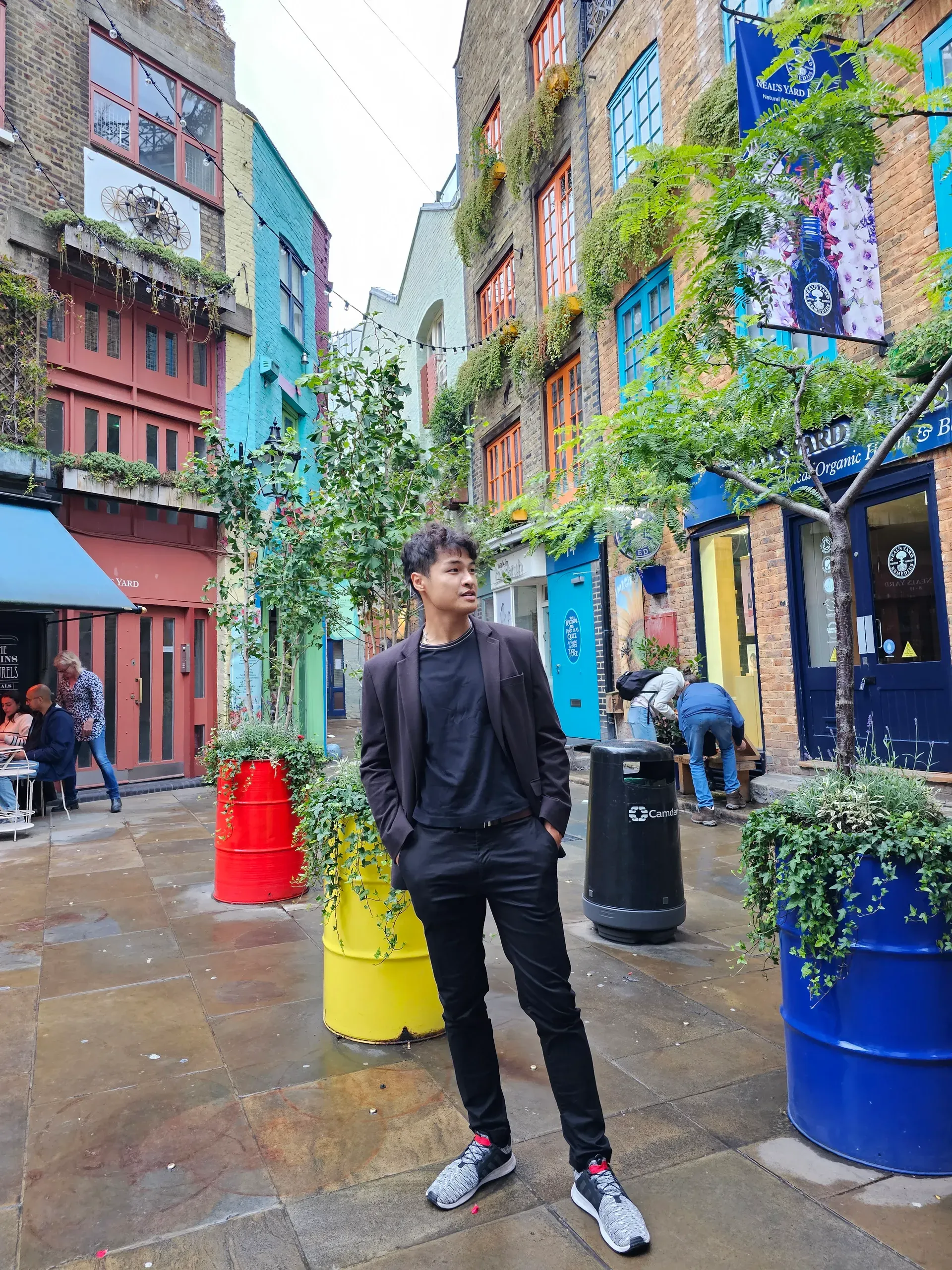 Neal’s Yard in Covent Garden: a narrow courtyard with colourful painted buildings, barrels used as planters, and people sitting at outdoor tables.