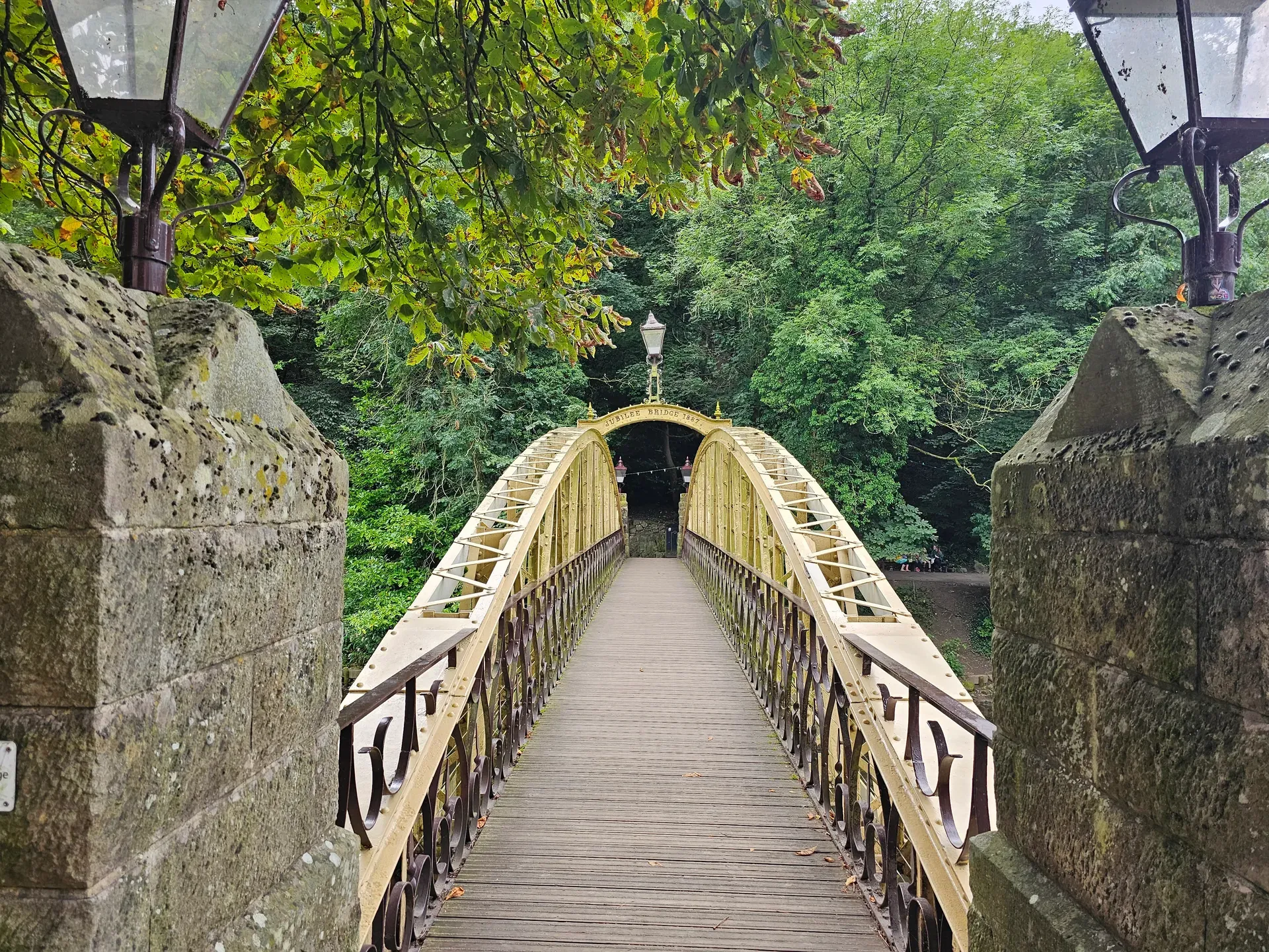 The yellow Jubilee Bridge of 1887 spans greenery with ornate iron railings and stone pillars.
